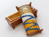 une poupée miniature représentant un homme allongé dans un lit, avec un bandage autour du cou