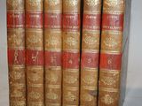 six old books are lined up in a row on a white surface