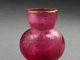 un vase en verre rose à bord doré posé sur une surface grise