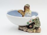 un petit oiseau perché dans un bol sur lequel est représentée une grenouille