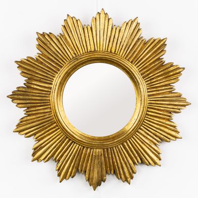 une photo d'un miroir doré en forme de soleil accroché au mur