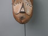 une image représentant un masque en bois posé sur un socle, sur fond gris