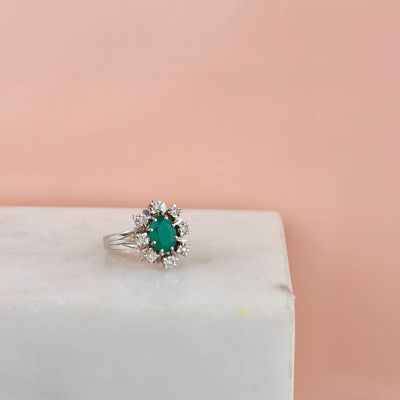 a close up of a green emerald and diamond ring on a white marble block