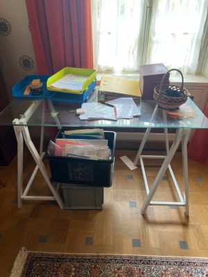 un bureau en verre sur lequel sont empilés de nombreux papiers