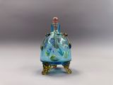 une bouteille en verre bleue ornée de fleurs, posée sur un socle