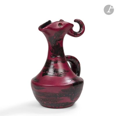 un vase rouge muni d'une anse en forme d'éléphant, posé sur une surface blanche