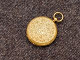 une image représentant une montre de poche en or posée sur un tissu marron