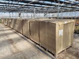 Plusieurs cartons sont empilés sur des palettes dans une serre remplie de plantes