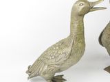 two metal ducks standing next to each other on a white surface