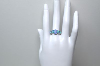 une main blanche à laquelle est passée une bague ornée de trois fleurs bleues