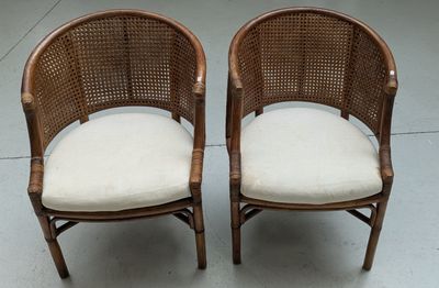 pair of wicker chairs with white cushions on a concrete floor