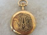 a gold pocket watch with a monogram on it