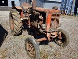 a rusted tractor sitting in a field next to a barn