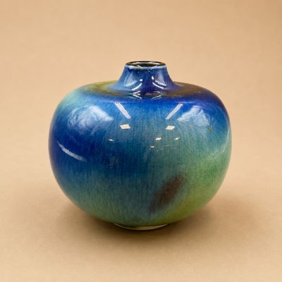 un vase bleu et vert posé sur une surface beige clair