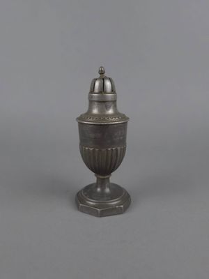 un vase en argent surmonté d'une clochette, posé sur une surface grise