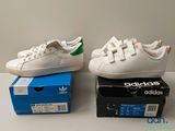 two pairs of white adidas sneakers sitting on top of a box