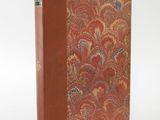 an old book with a red cover sitting on top of a white surface