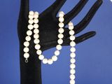 la main d'une femme tenant un collier et un bracelet de perles blanches