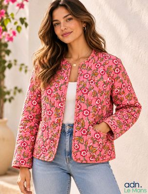 a woman wearing a pink jacket and jeans standing in front of a white wall