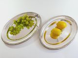 two oval silver trays with lemons and grapes on them