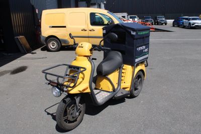 un scooter garé sur un parking, avec une camionnette jaune en arrière-plan