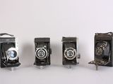 three old cameras sitting side by side on a white surface