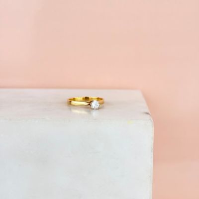 une bague de fiançailles en or sertie d'un diamant, posée sur un bloc de marbre blanc