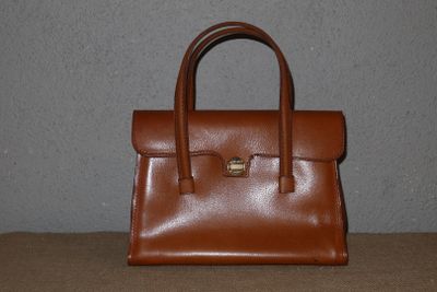un sac à main en cuir marron posé sur une table devant un mur gris