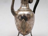 une théière ancienne en argent, dotée d'une anse noire, posée sur un socle