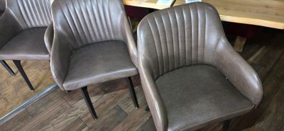 three brown leather chairs sitting in front of a wooden table