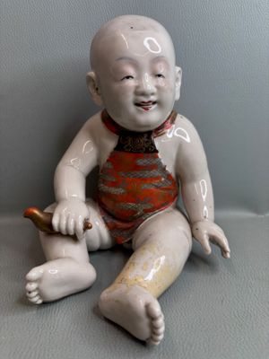 une poupée assise par terre, une brosse à dents dans la main