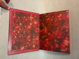a hand holding a red book open on a table