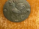 a silver coin with a rooster on it on a wooden surface