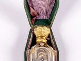 un petit flacon de parfum dans un étui vert posé sur une surface blanche