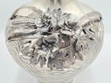 a silver vase with flowers and leaves on it