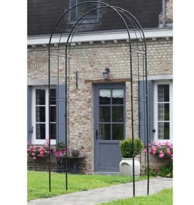Une arche en métal noir se dresse devant un bâtiment en briques
