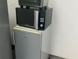 three microwaves stacked on top of each other next to a refrigerator