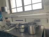 Des casseroles et des poêles sont posées sur un plan de travail en acier inoxydable dans une cuisine