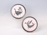 deux assiettes roses et noires ornées d'oiseaux, posées sur une surface blanche
