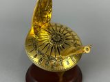 a gold sundial on a wooden stand with a white background