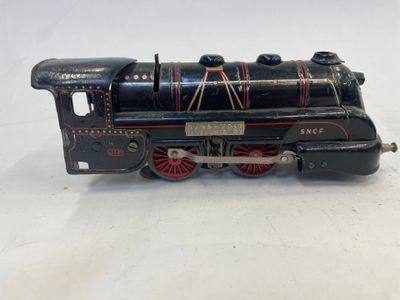 une vieille locomotive de jouet noire avec des roues rouges, posée sur une surface blanche