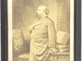 une vieille photo d'un homme en costume debout devant une chaise