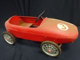 an old red pedal car sitting on top of a black surface