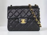 un sac Chanel noir muni d'une chaîne dorée, posé sur une table blanche