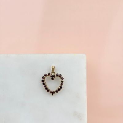 un pendentif en forme de cœur en or, orné de grenats, repose sur un bloc de marbre