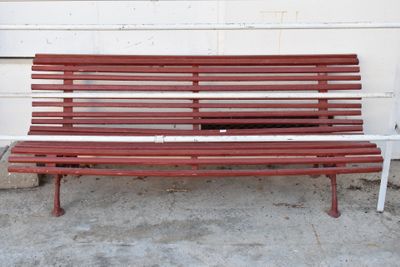 un banc rouge posé sur le trottoir, à côté d'un immeuble blanc