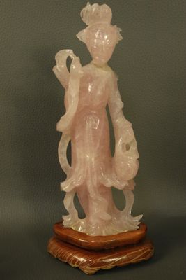 une statue en jade rose représentant une femme tenant un oiseau, posée sur un socle en bois