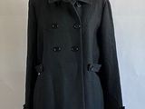 black peale coat on a mannequin stand against a white wall