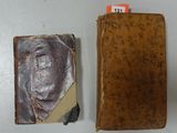 an old book sitting on top of a white table next to a brown book
