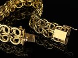 a gold bracelet with a gold clasp on a black surface